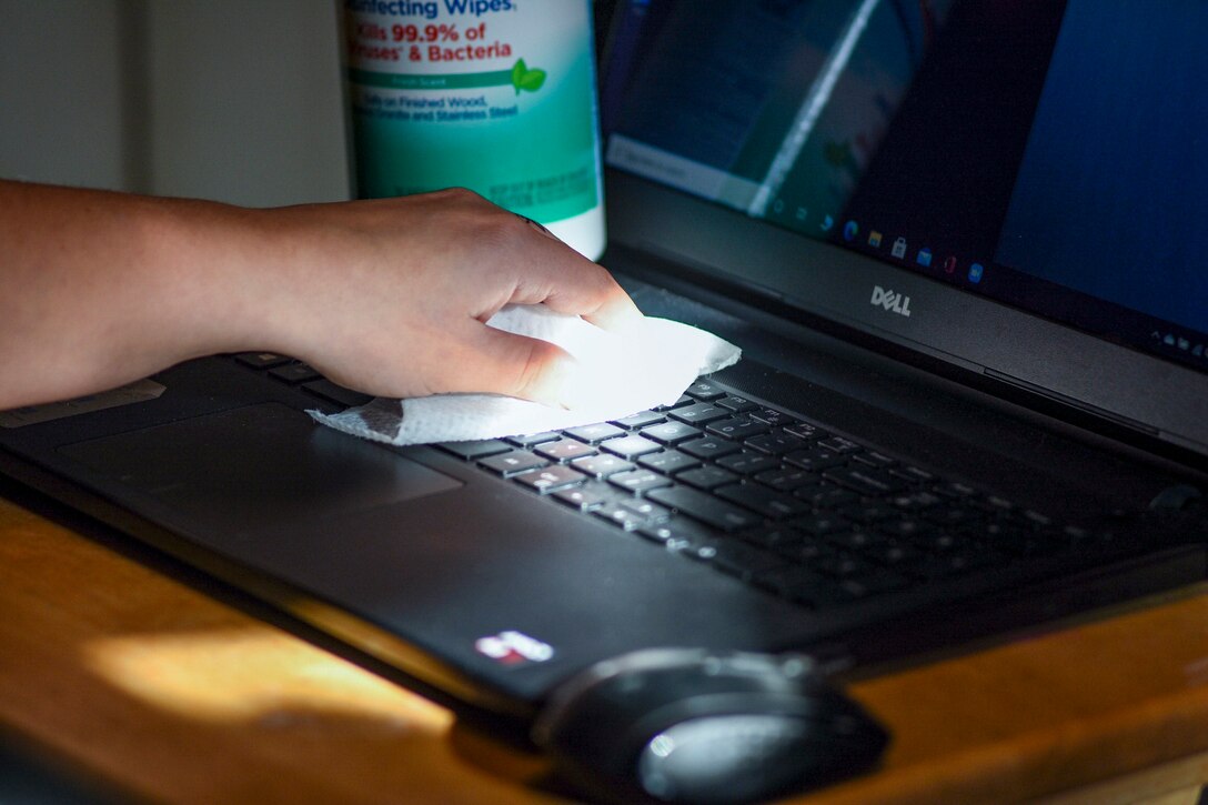 A person's hand uses a wipe to clean a laptop keyboard.