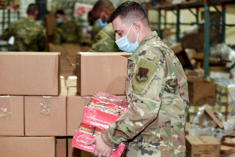 A National Guard soldier carries cases of peanut butter in front