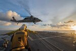 Sailors signal to MH-60S Sea Hawk helicopter as it hovers over flight deck of USS McCampbell