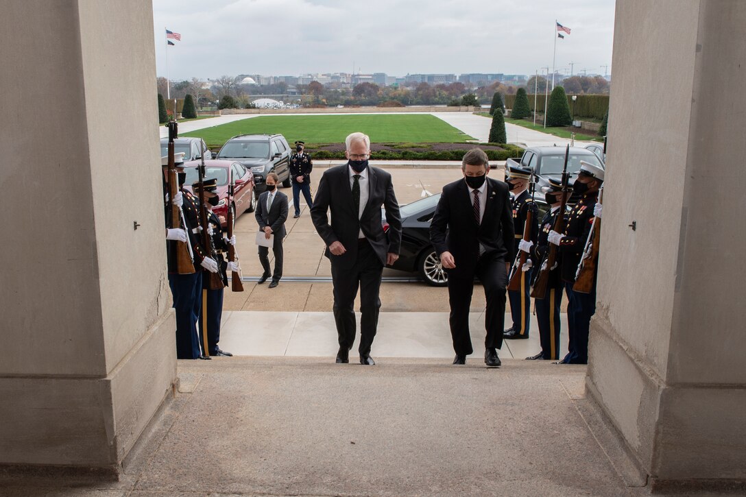 Two men walk up the stairs outside of a large building. An honor guard lines their path.