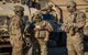 Three Airmen stand in front of vehicles and talk.