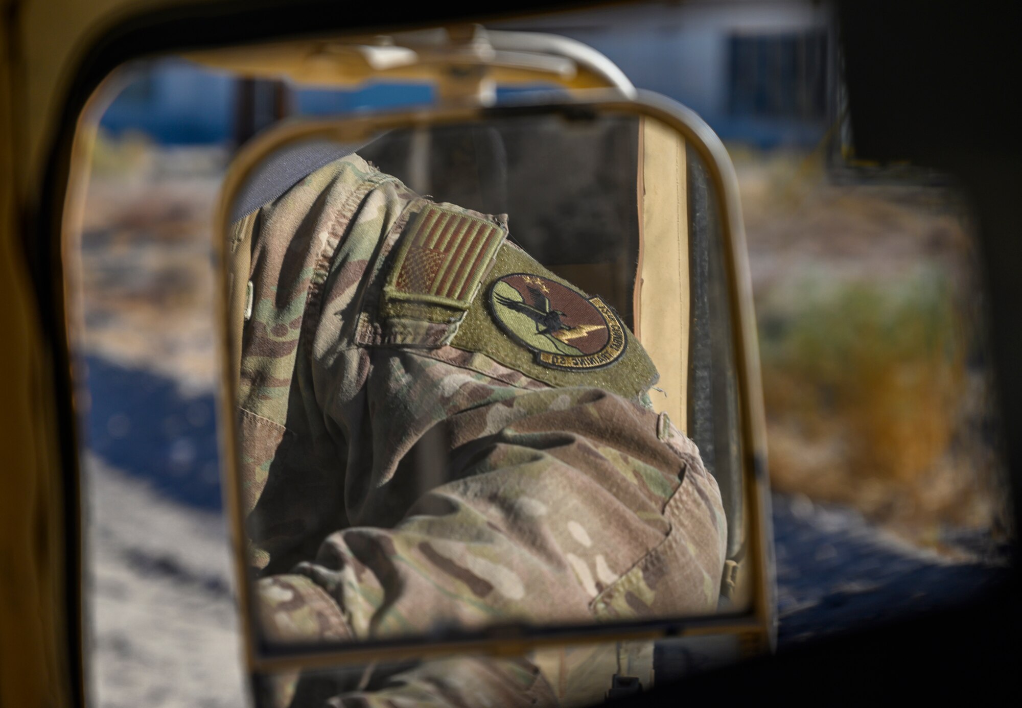 Arm of an Airman reflected in a side-view mirror of a Humvee.