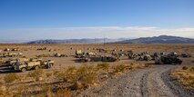 Military vehicle and tents at the bottom of a road in the desert.