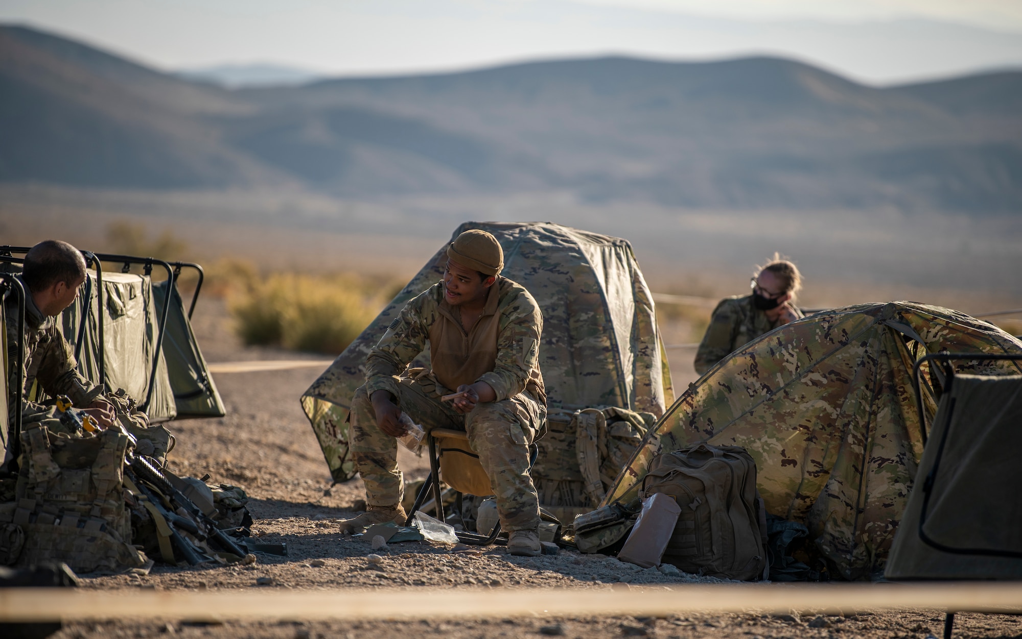 Airmen and Soldiers sit in front of tents eating MREs.