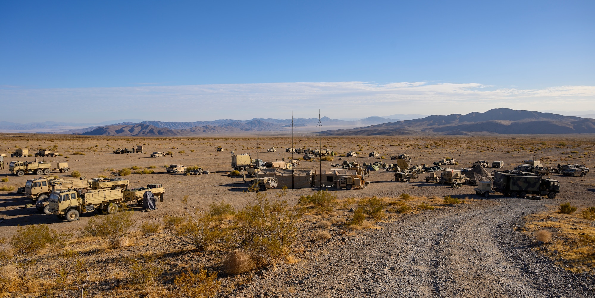 Military vehicle and tents at the bottom of a road in the desert.