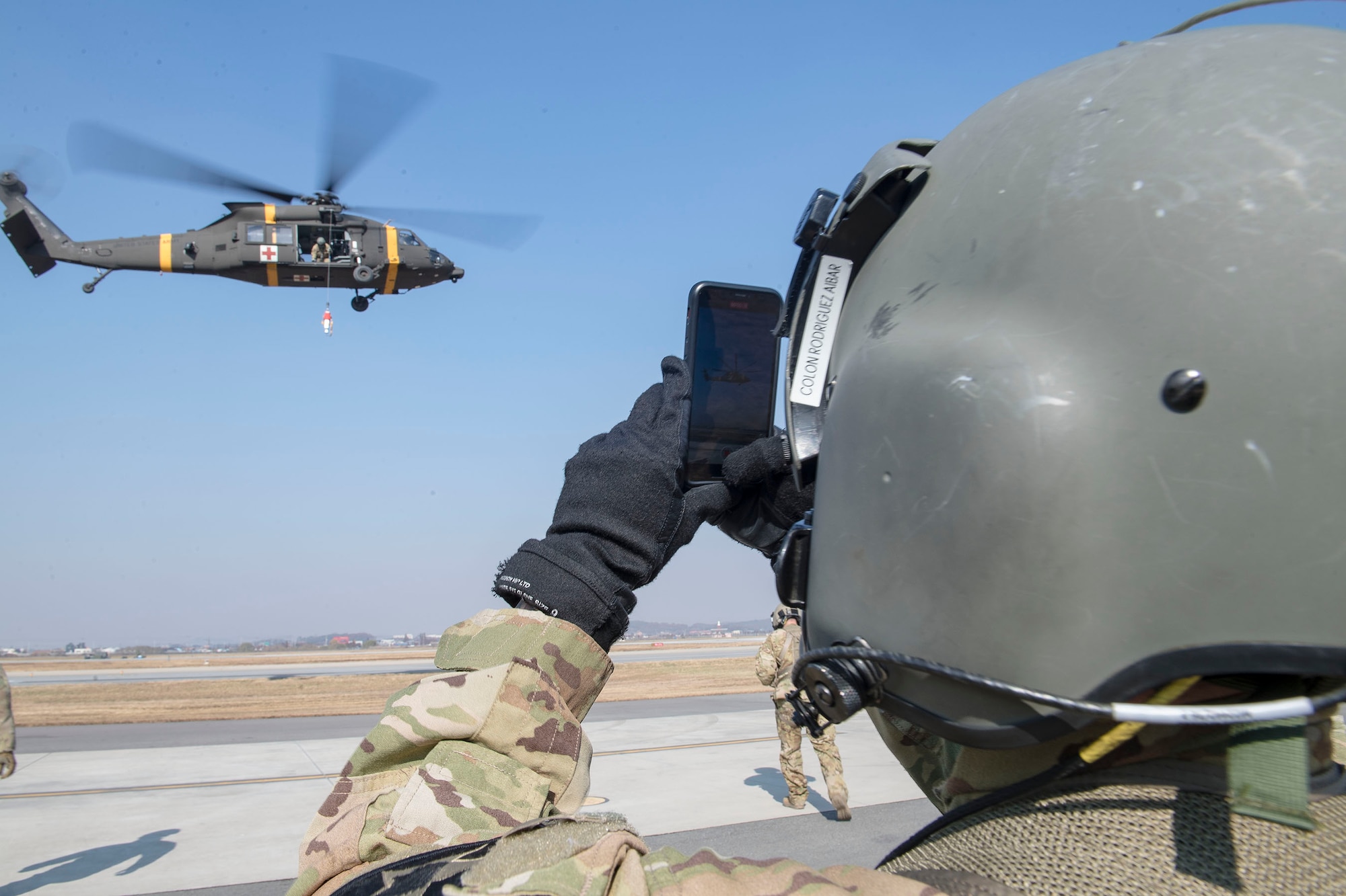 An HH-60m aircrew member from U.S. Army Garrison Humphreys 3-2 General Support Aviation Battalion takes a pause to photograph hoist operations on the flightline at Osan Air Base, Republic of Korea, Nov. 12, 2020. Osan’s 51st Fighter Wing Survival, Evasion, Resistance and Escape trainers and the 3-2 GSAB partnered to test individual’s high-risk survival readiness. (U.S. Air Force photo by Senior Airman Greg Nash)