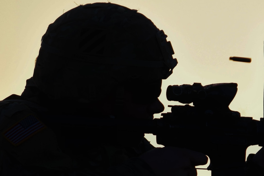 A soldier seen in silhouette fires his weapon.
