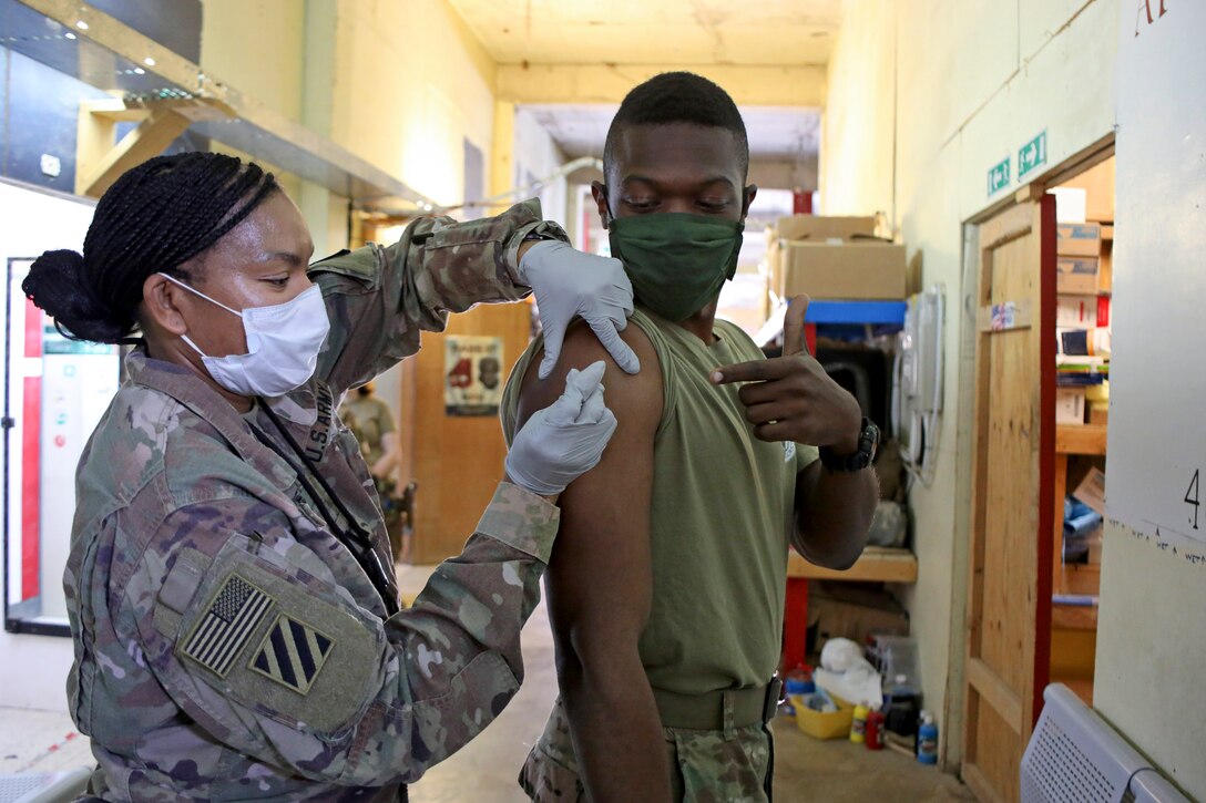 A soldier gives another soldier a shot while they are standing.