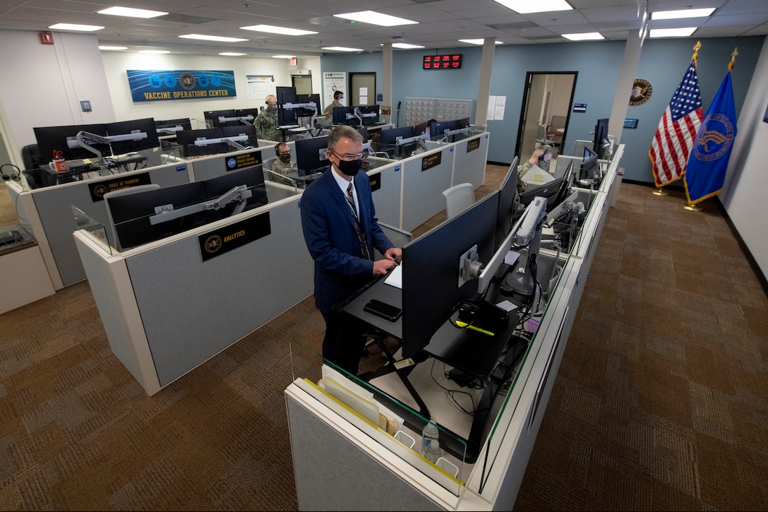 A man wearing a mask stands in front of a computer.