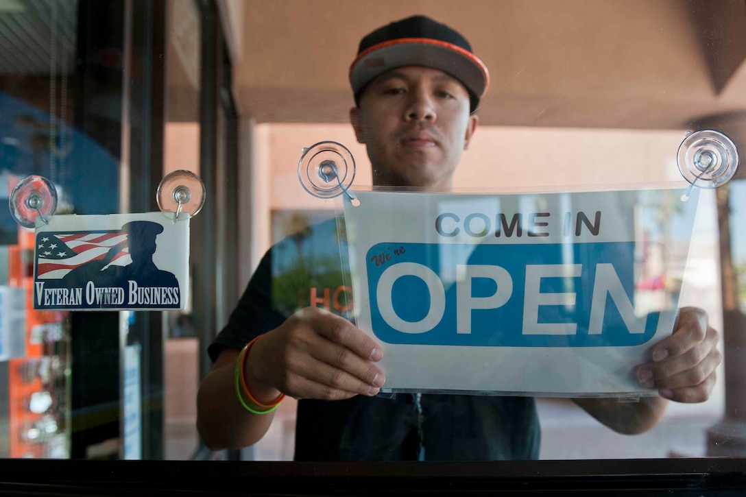 A man places an "open" sign on a glass door.