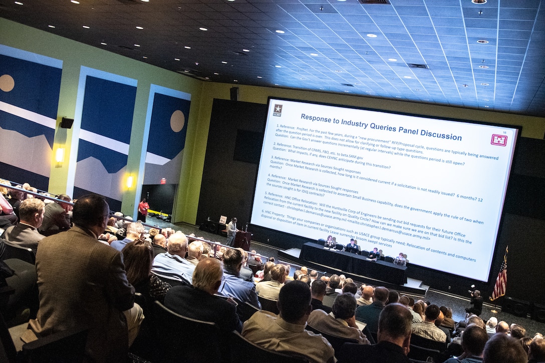 Hundreds of individuals sit in an auditorium and look at a slide presentation.