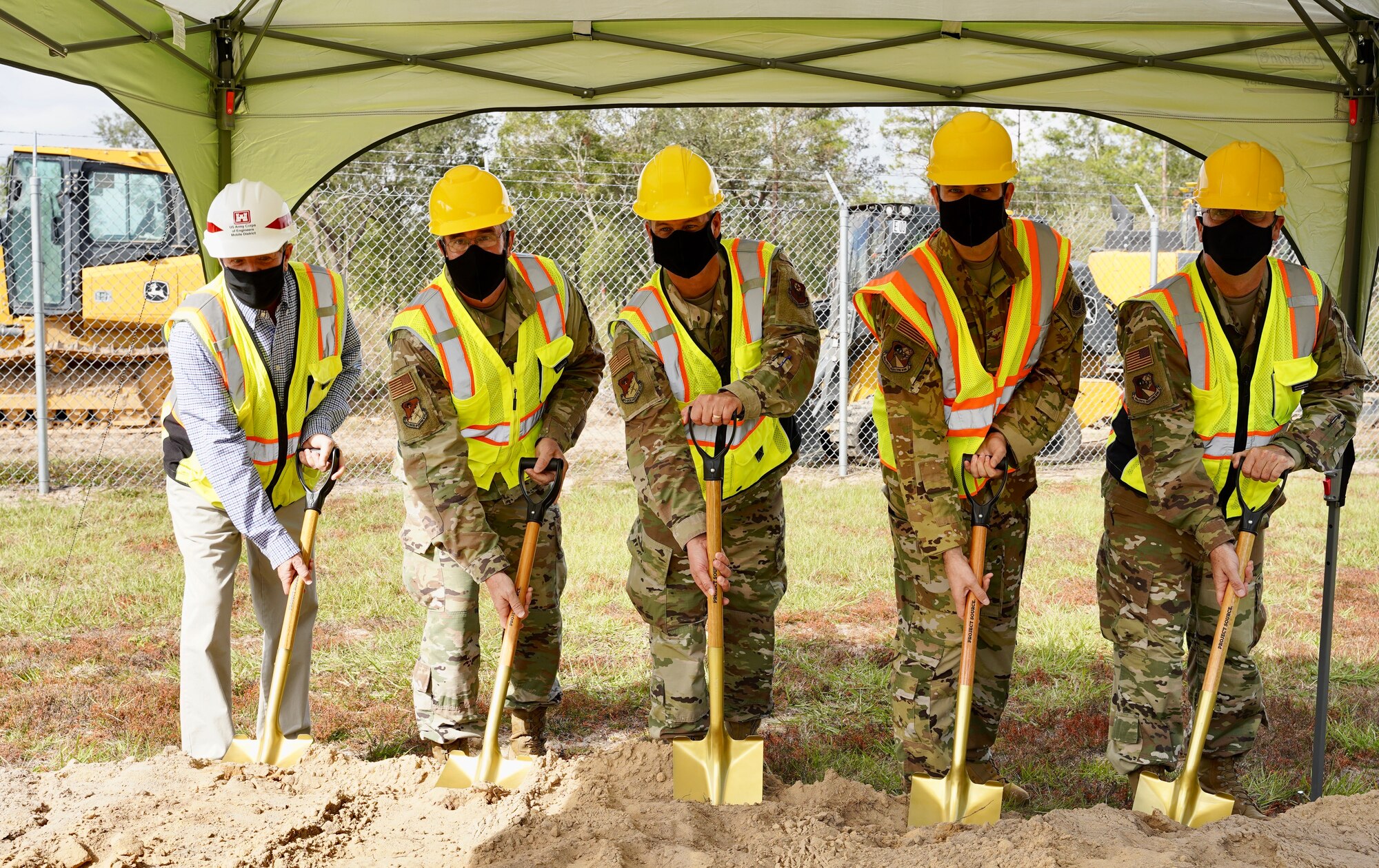 Photo of five people standing with shovels next to a dirt mound