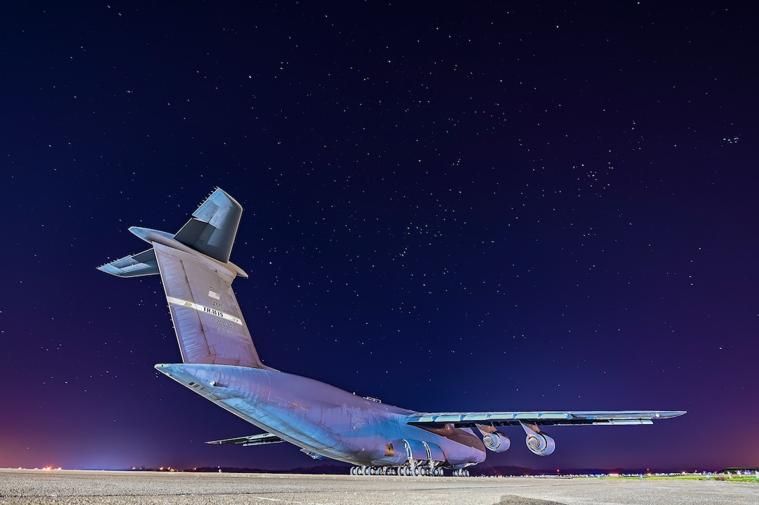 A very large grey airplane sits on the flight line under the stars.