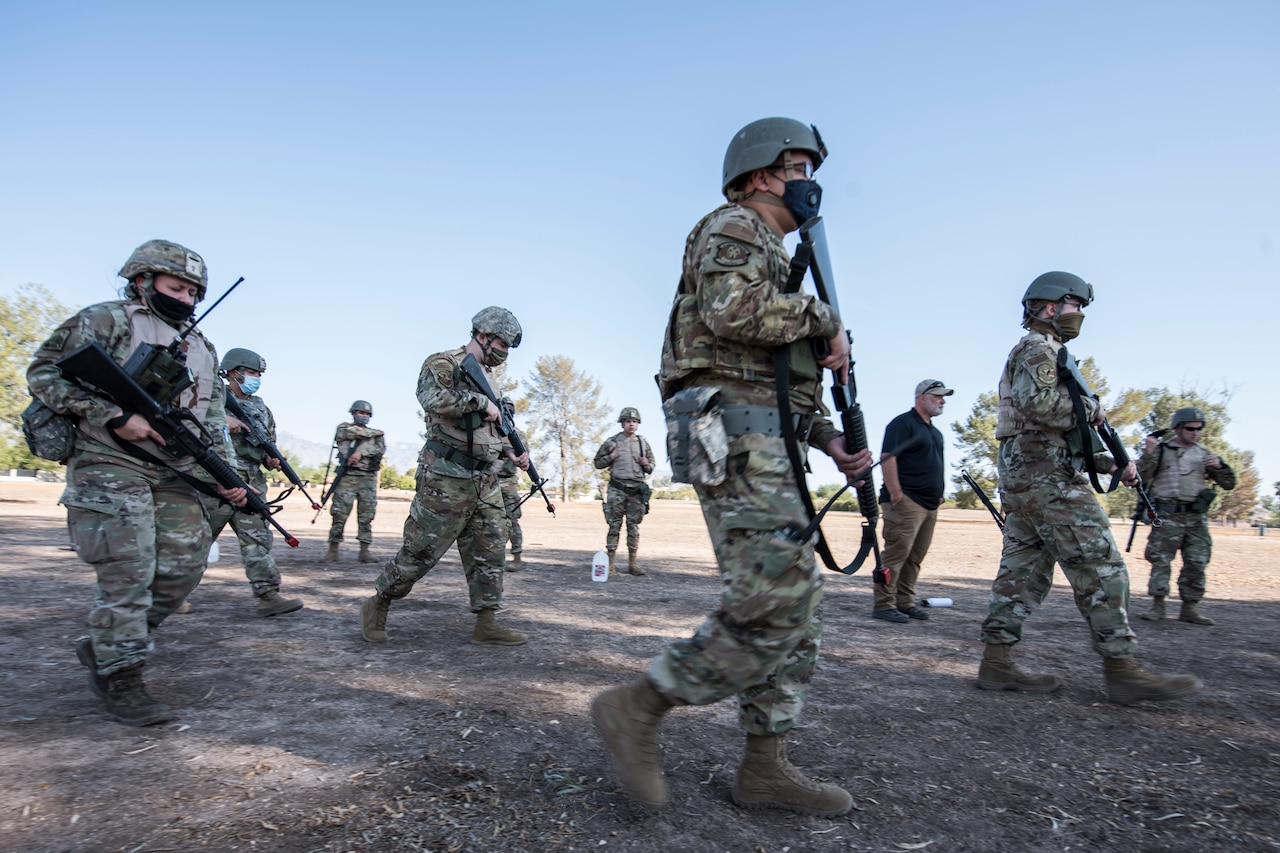 Airmen move through a field while holding weapons.
