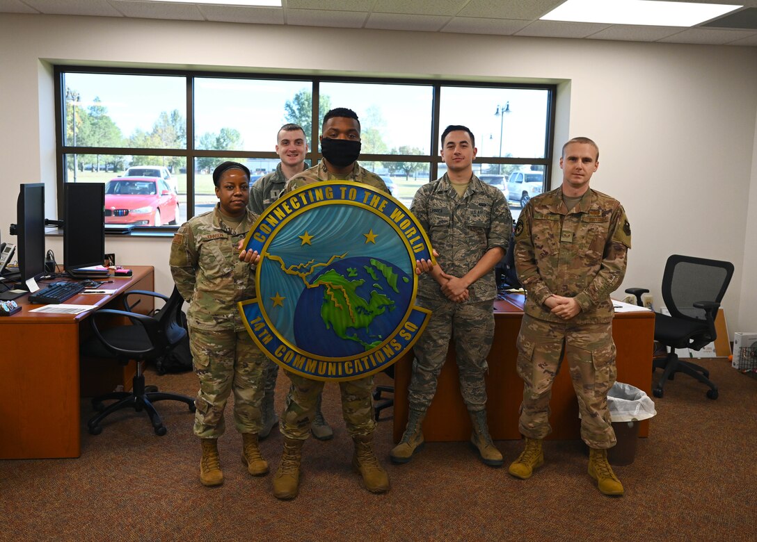 U.S. Air Force Airmen of the 14th Communications Squadron Client Systems Technician shop, pose with their squadron logo Nov. 2, 2020, on Columbus Air Force Base, Miss. The CST shop has successfully updated over a 1,000 devices with outdated Basic Input Output Systems base wide. (U.S Air Force photo by Senior Airman Jake Jacobsen)