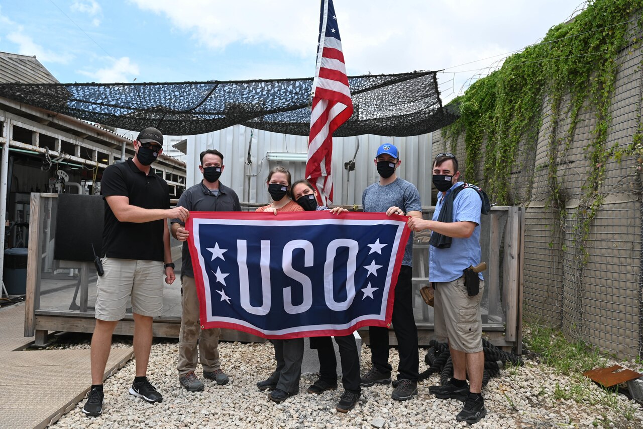 Men and women pose with a USO flag while in front of a U.S. flag.