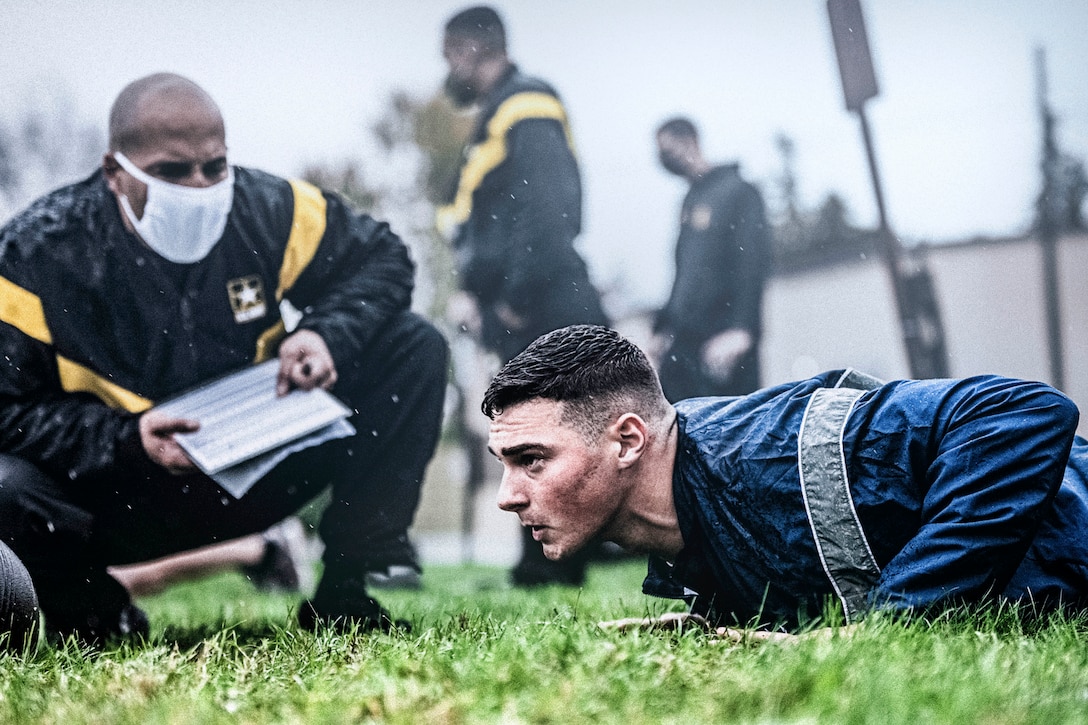 An airman performs a pushup in front of a soldier.