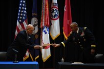 Two men signing contractual agreement on a stage.