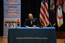 Two men signing contractual agreement on a stage.