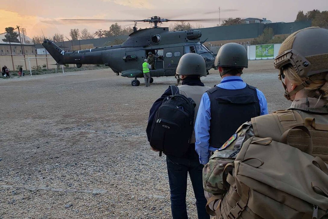 Three people with helmets line up near a helicopter.