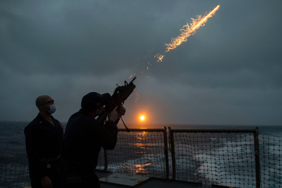 A sailor fires a flare in front of another sailor.