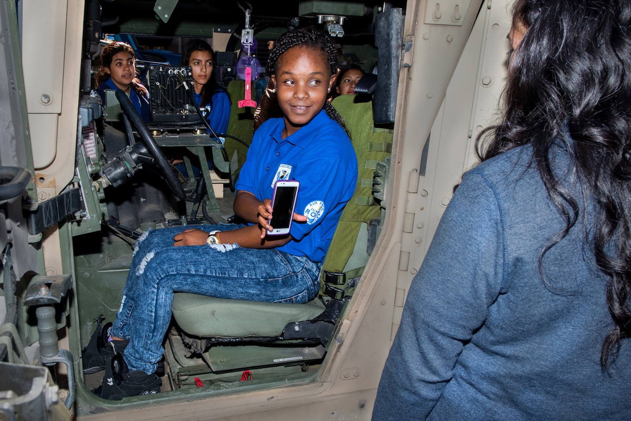 A young girl sits inside a military vehicle.