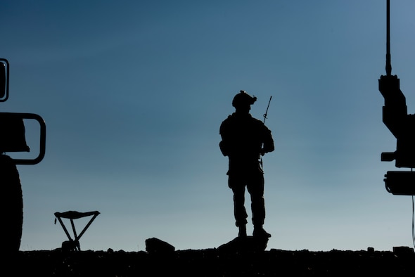 Airman stands on a hill and talks on the radio.