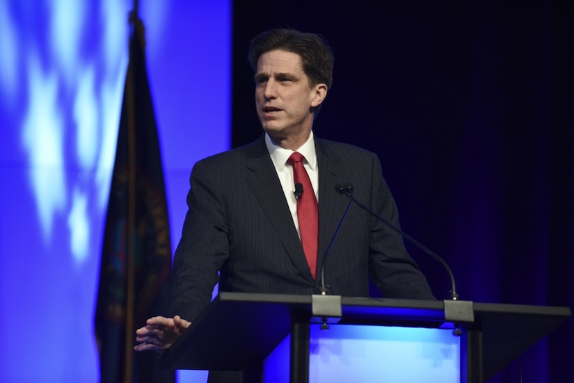 A man in a business suit stands at a lectern.