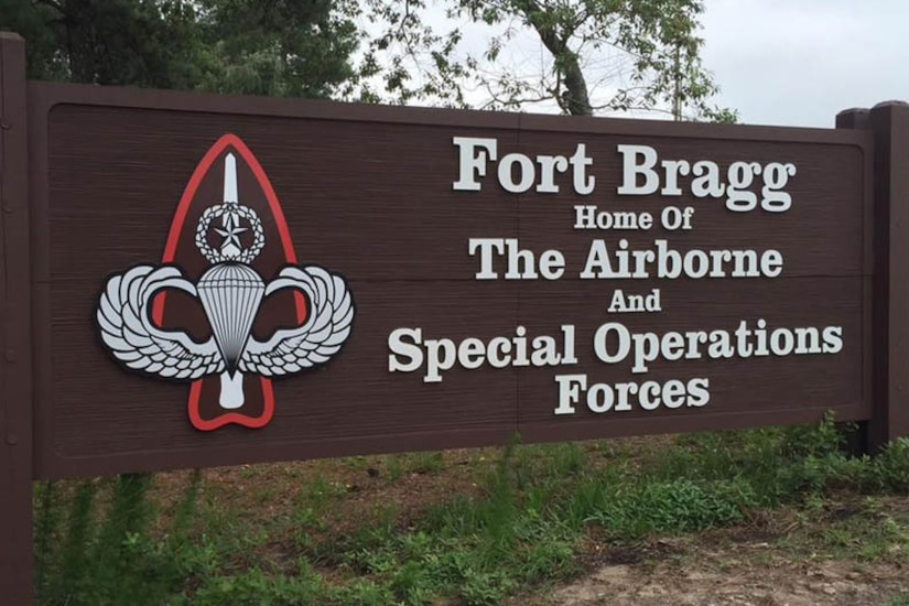 A brown horizontal outdoor sign says "Fort Bragg Home Of The Airborne And Special Operations Forces"