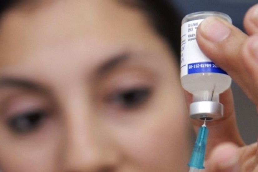 A woman uses a syringe to extract liquid from a small bottle she's holding upside down.