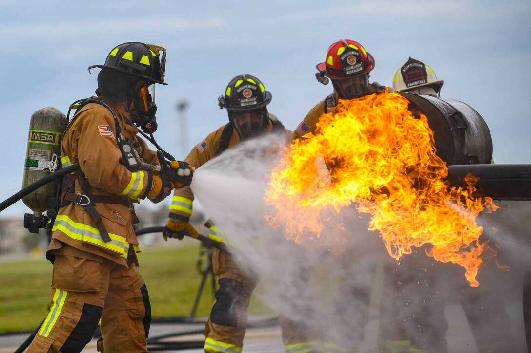 Three airmen use a hose to spray water onto an aircraft fire.