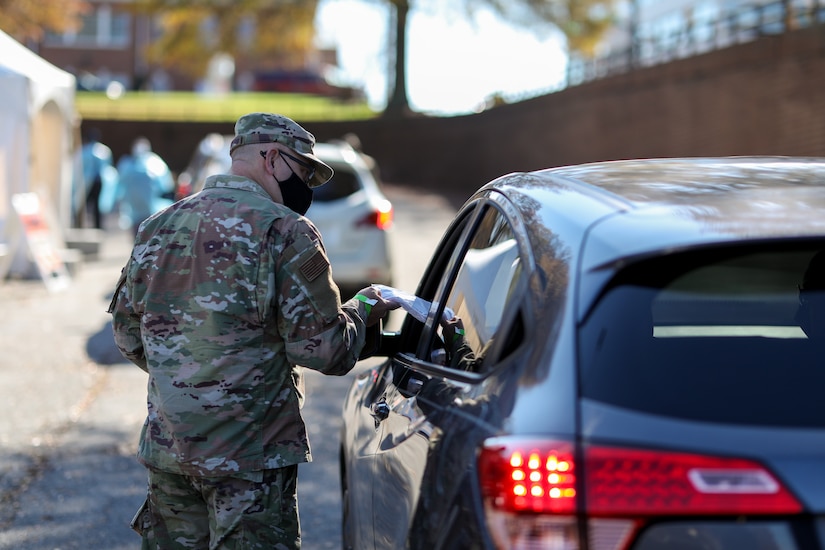 A soldier hands out masks to people in a car at a drive-thru testing site.