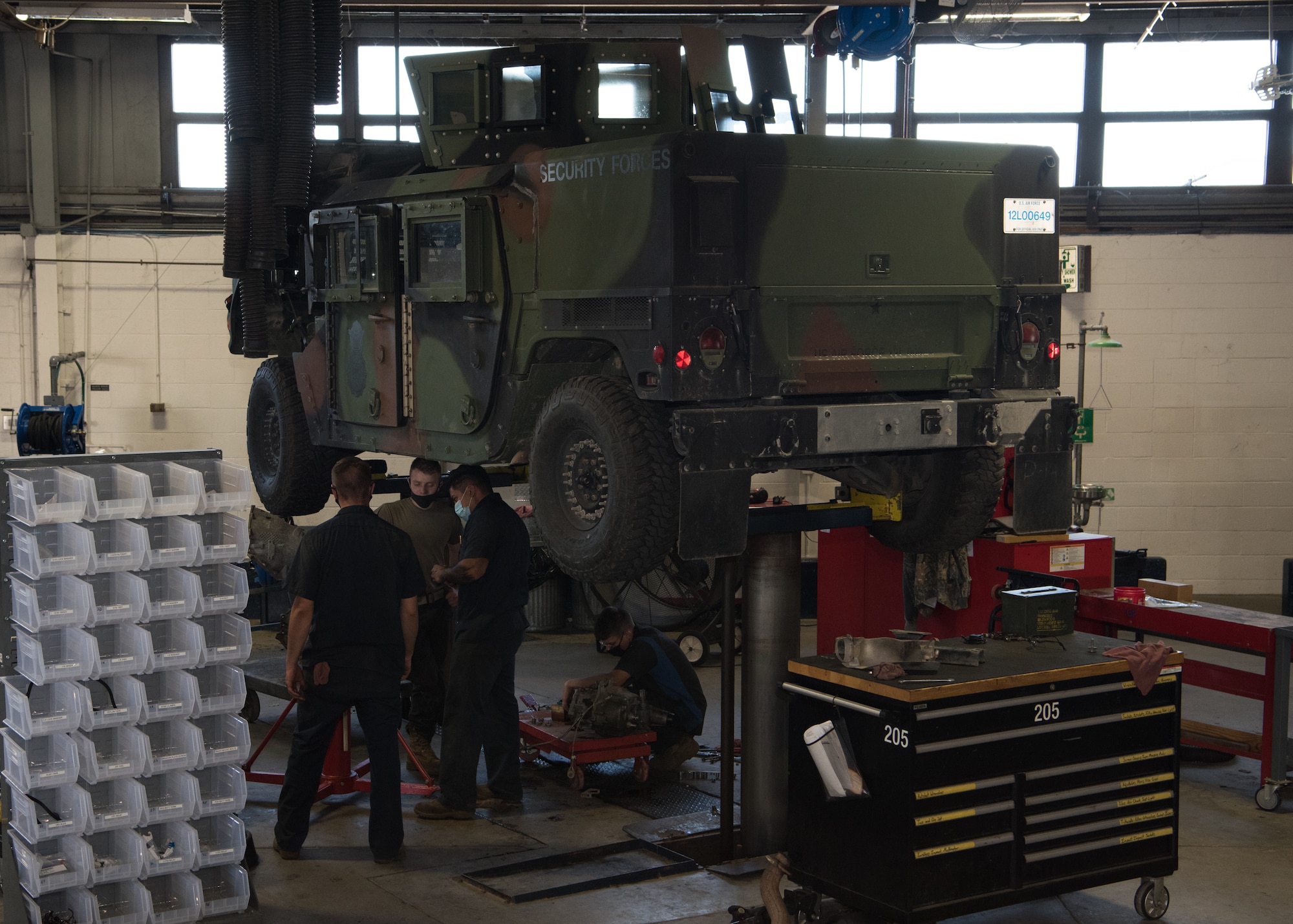 Airmen work and stand under a Humvee in the low bay of vehicle maintenance.