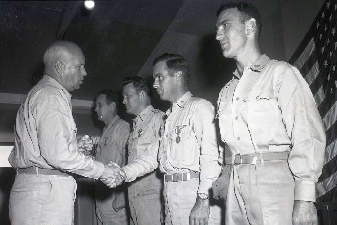 A man shakes the hand of a man facing him, who is lined up beside three other men.