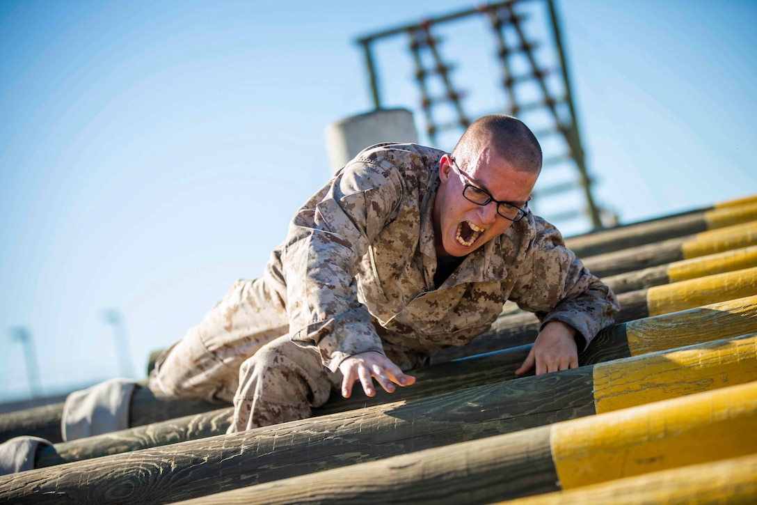 A Marine Corps recruit climbs over a wooden obstacle.