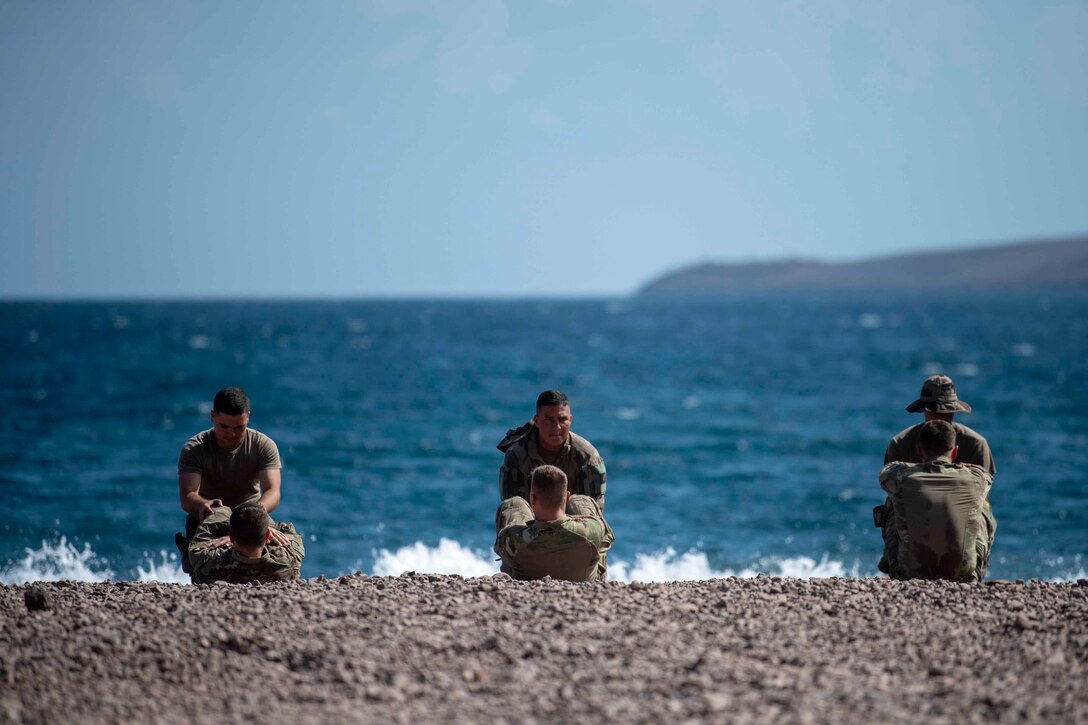 Soldiers do situps on a beach.