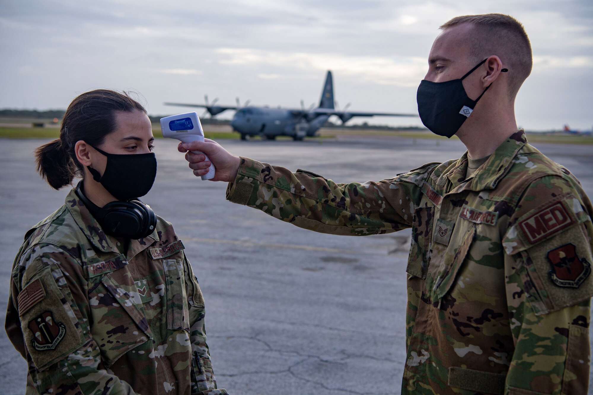 An Airman takes the temperature of another Airman in front of a C-130.