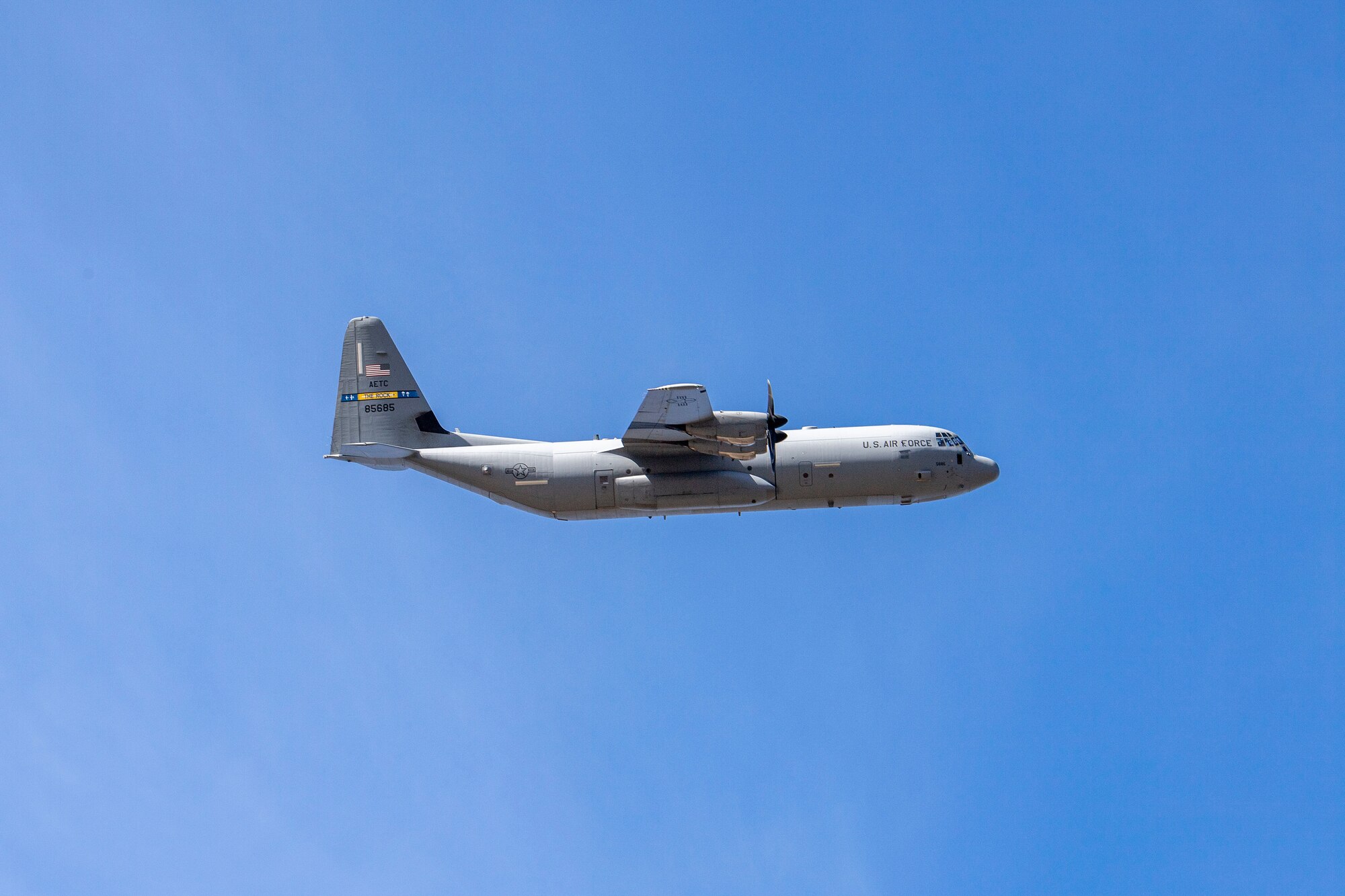 A C-130J Super Hercules flies over a dirt landing zone.
