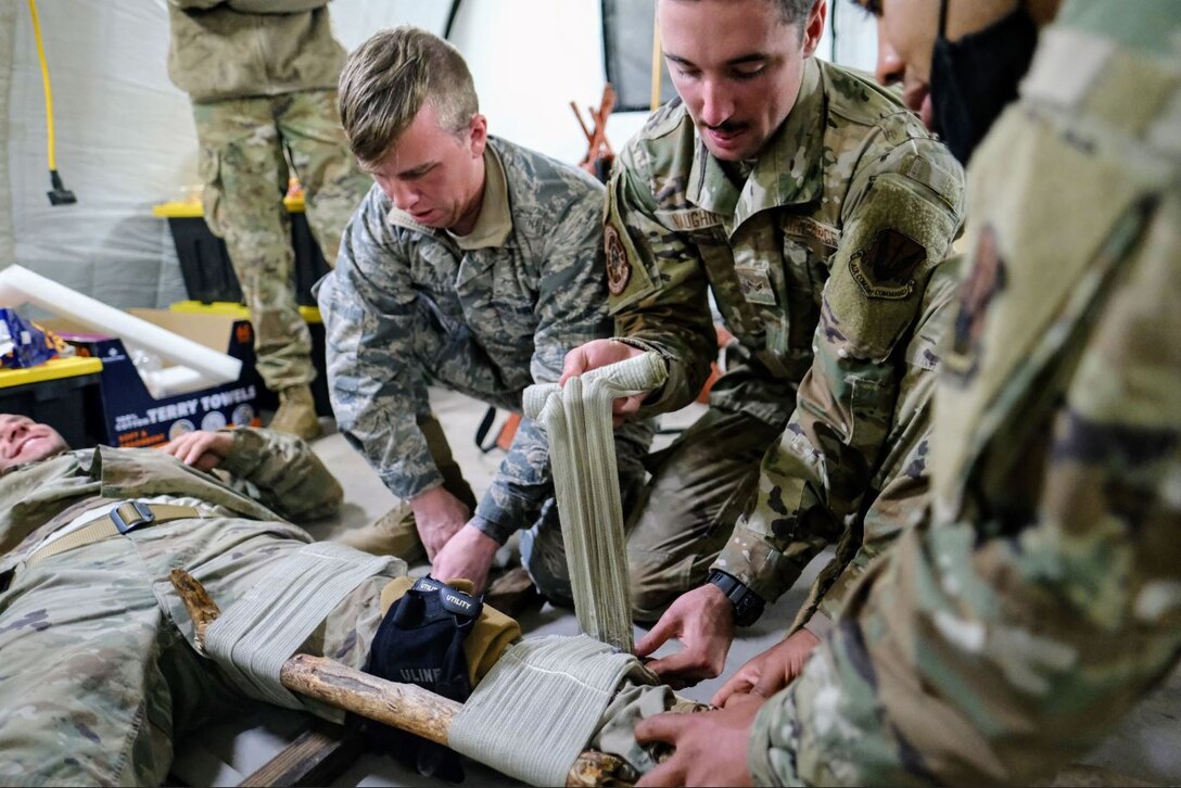 Airmen in the 729th Air Control Squadron practice self-aid and buddy care by wrapping a bandage on a simulated injured patient's leg.