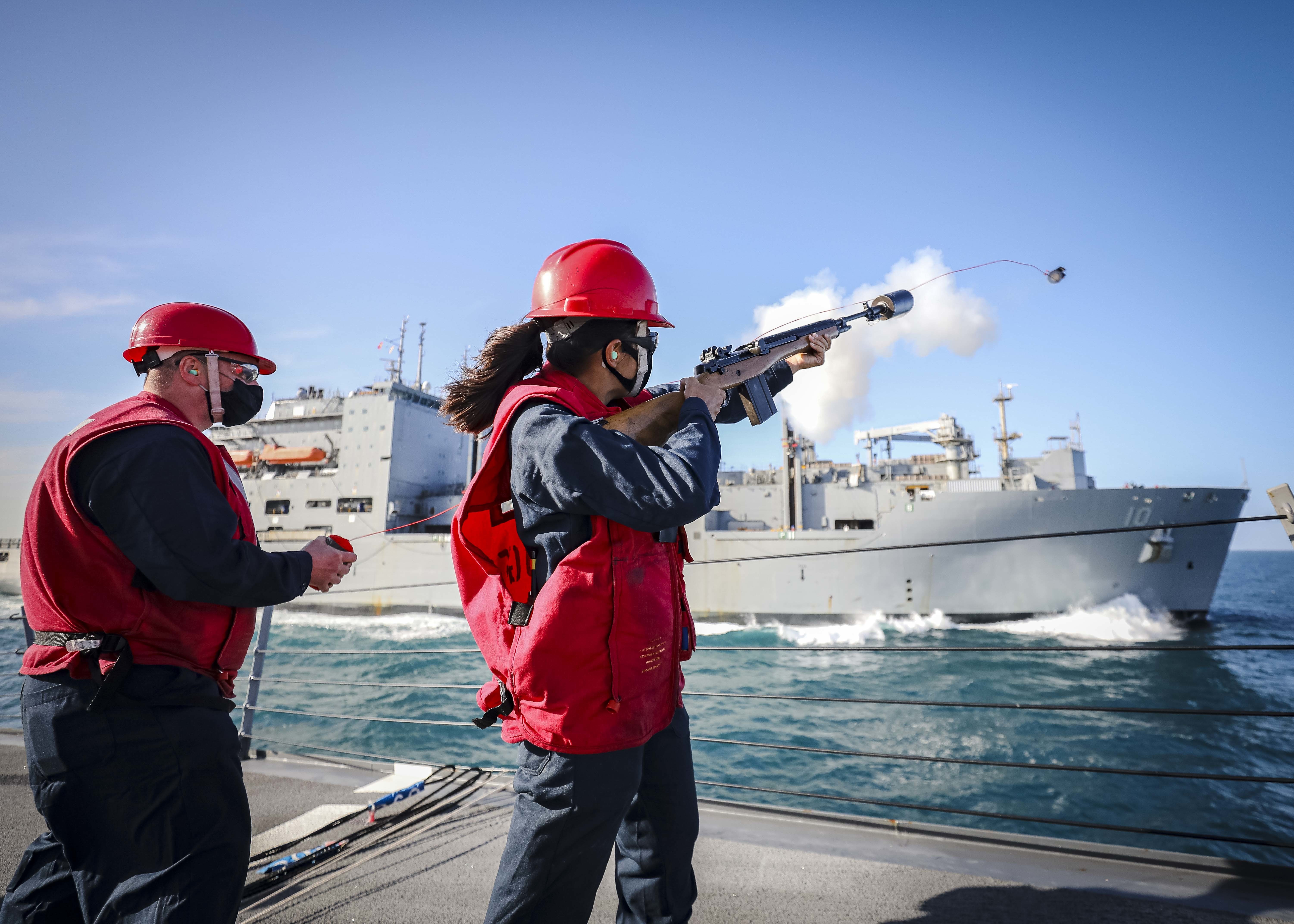 A Sailor fires a shot line from the foc's'le aboard the Arleigh Burke-class guided-missile destroyer USS John S. McCain (DDG 56) towards the Lewis and Clark-class dry cargo and ammunition ship USNS Charles Drew (T-AKE 10)