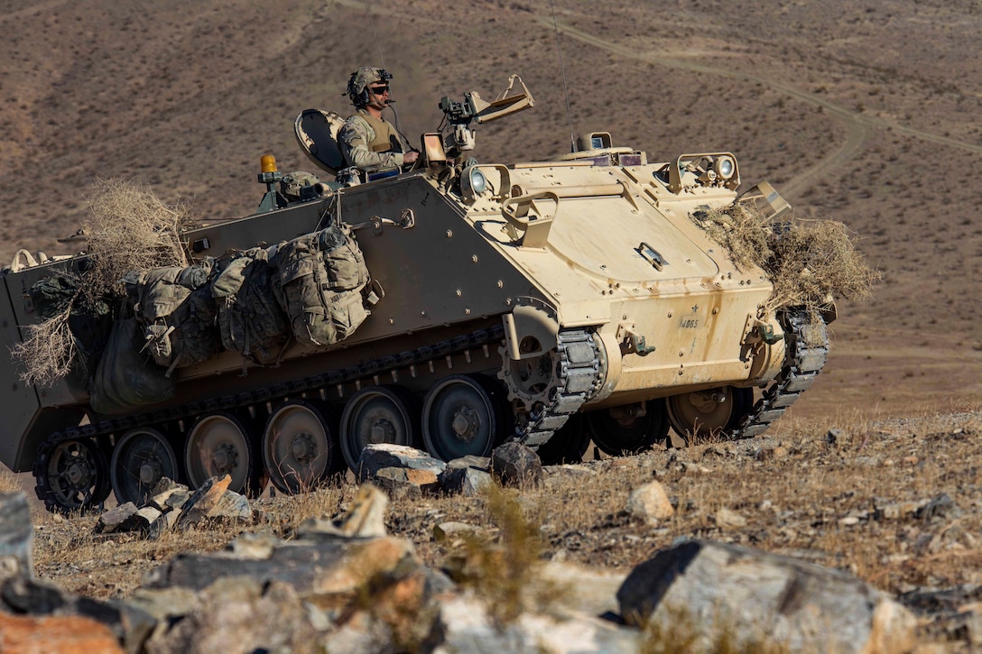 A soldiers rides in a vehicle in a desert-like area.