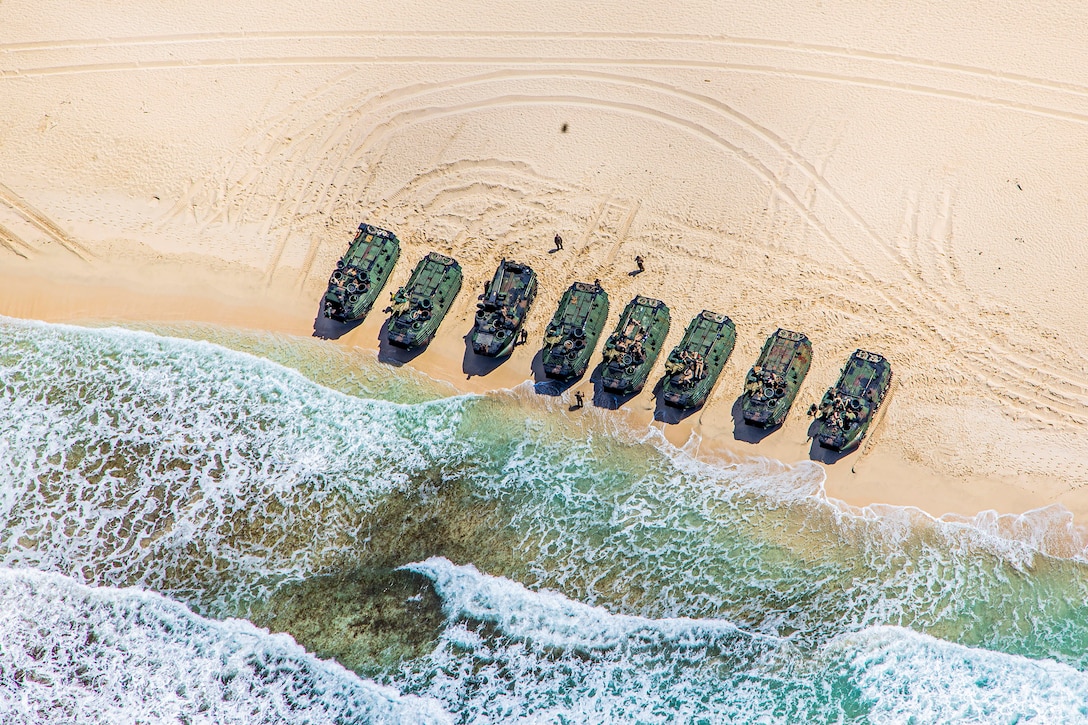 Eight vehicles in a row on a  beach are seen from above.