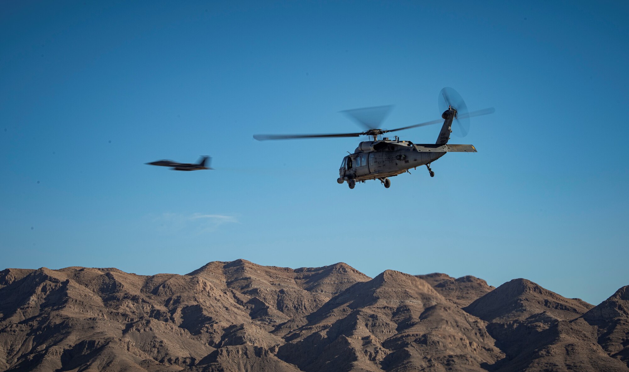 A helicopter flies over mountains with a jet in the background