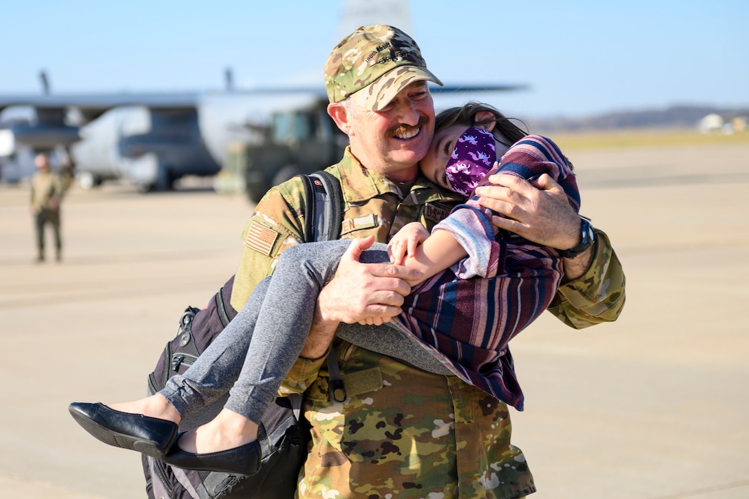 A smiling airman holds a smiling child on a flightline