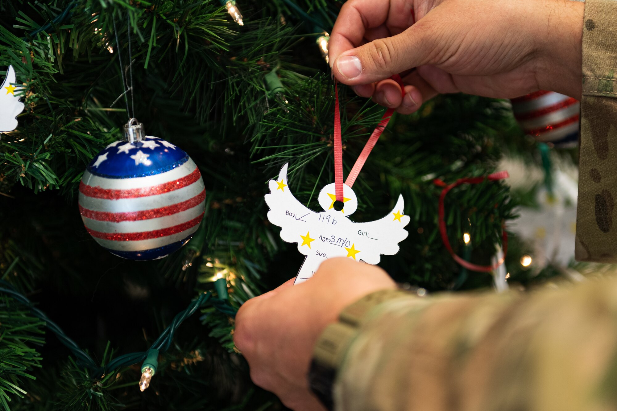 A photo of an Airman hanging an ornament on a tree
