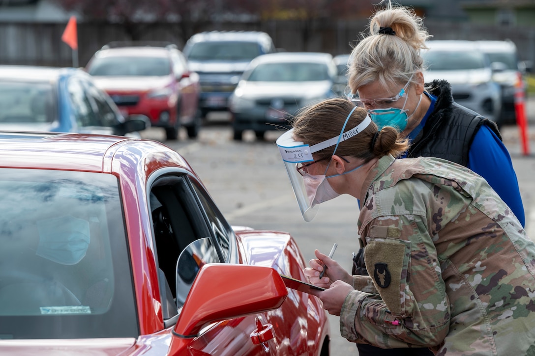 A soldier holding a clipboard speaks to a motorist.