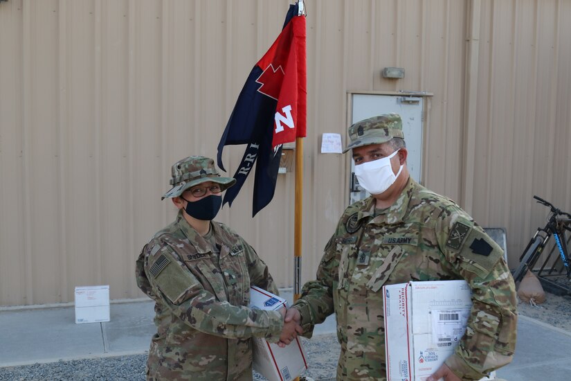 U.S. Army 1st Sgt. Frank Palfrey, right, awards a challenge coin to Sgt. Hope Snyder, mailroom clerk for Headquarters and Headquarters Company, 28th Expeditionary Combat Aviation Brigade, for her efforts in distributing over 100 care packages to HHC Soldiers.
