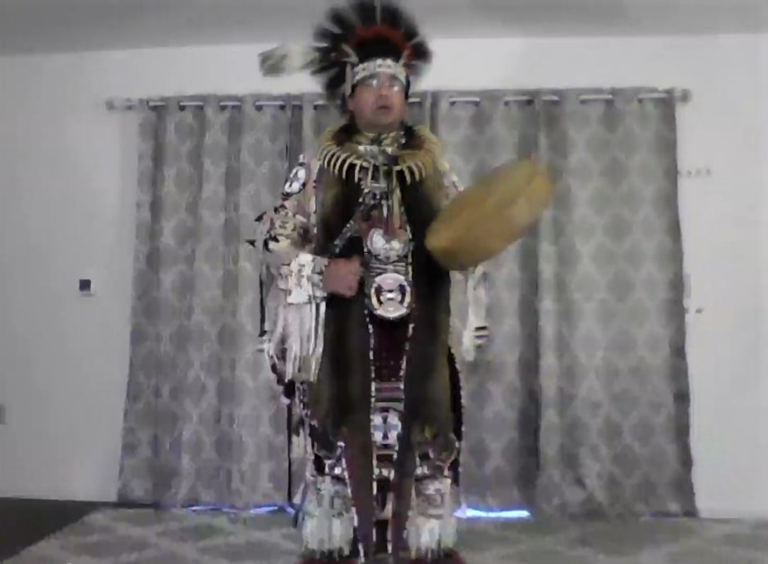 A Native American man wearing traditional garb performs a dance.