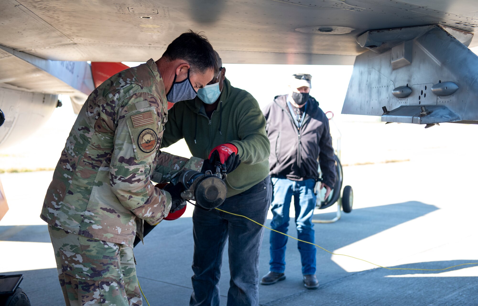 U.S. Air Force colonel is handed fuel hose from U.S. Air Force contractor under the wing of a QF-16 aircraft after refueling.