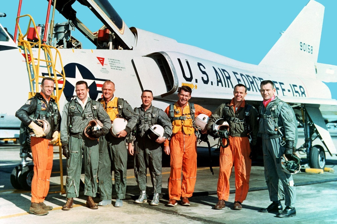 Seven people in flight suits stand in front of an aircraft on a flightline.